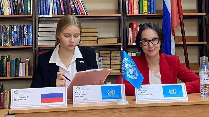 На изображении Студенты участвуют в заседании международной организации, работая с документами за столом переговоров в учебной аудитории