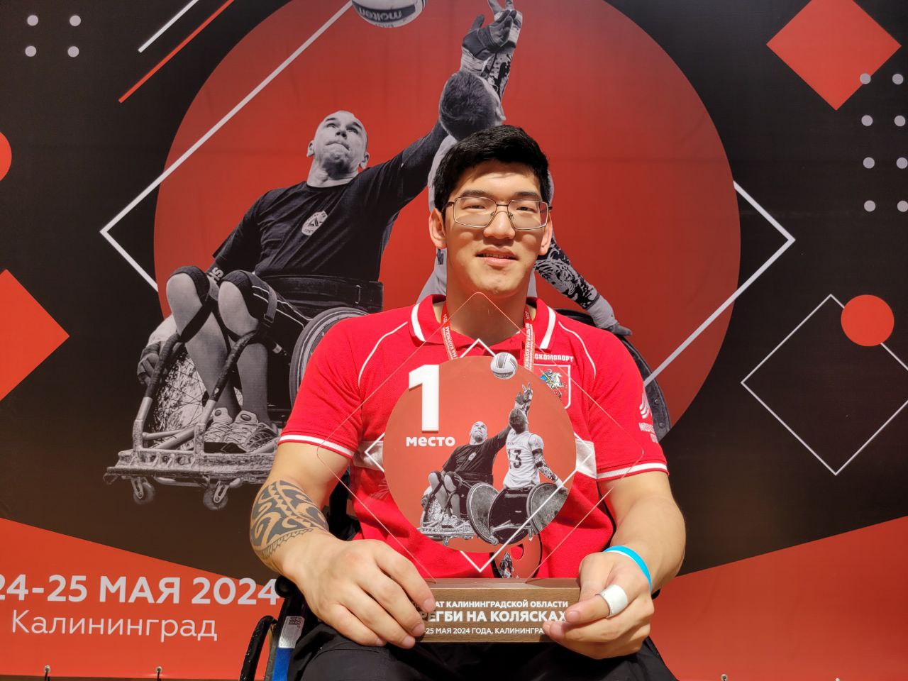 Photo pop-up. Sur le cliché — le champion de la compétition « RUGBY EN FAUTEUIL ROULANT » à Kaliningrad. L'élément central est un chiffre 1 éclatant, symbolisant la première place. Le sportif est en fauteuil roulant et photographié avec sa récompense. L'image transmet la joie, la force, le respect de l'exploit et l'esprit de dépassement de soi dans le sport.
