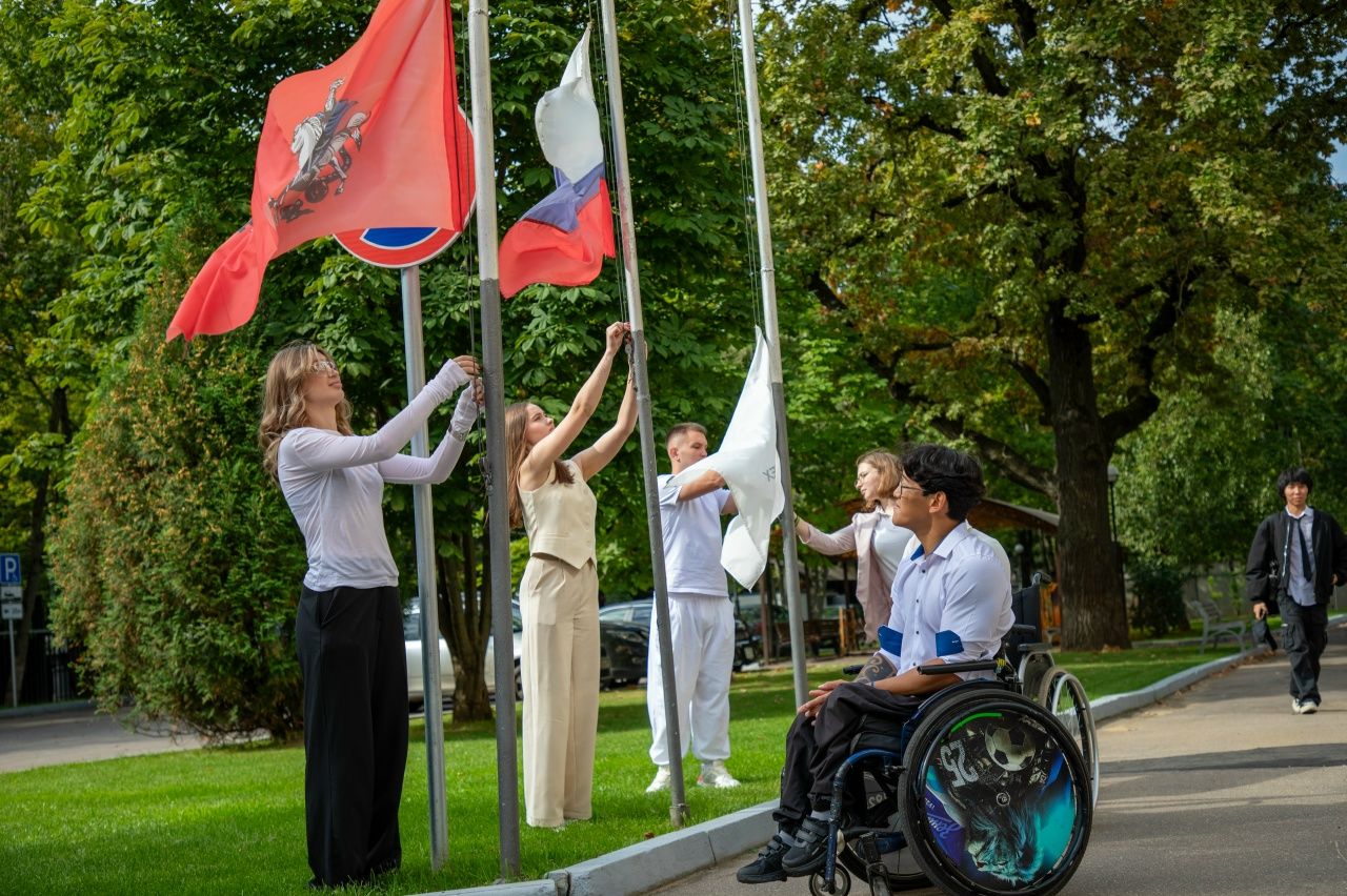 RSU students, including a guy in a sports wheelchair, are raising flags on flagpoles on a green lawn