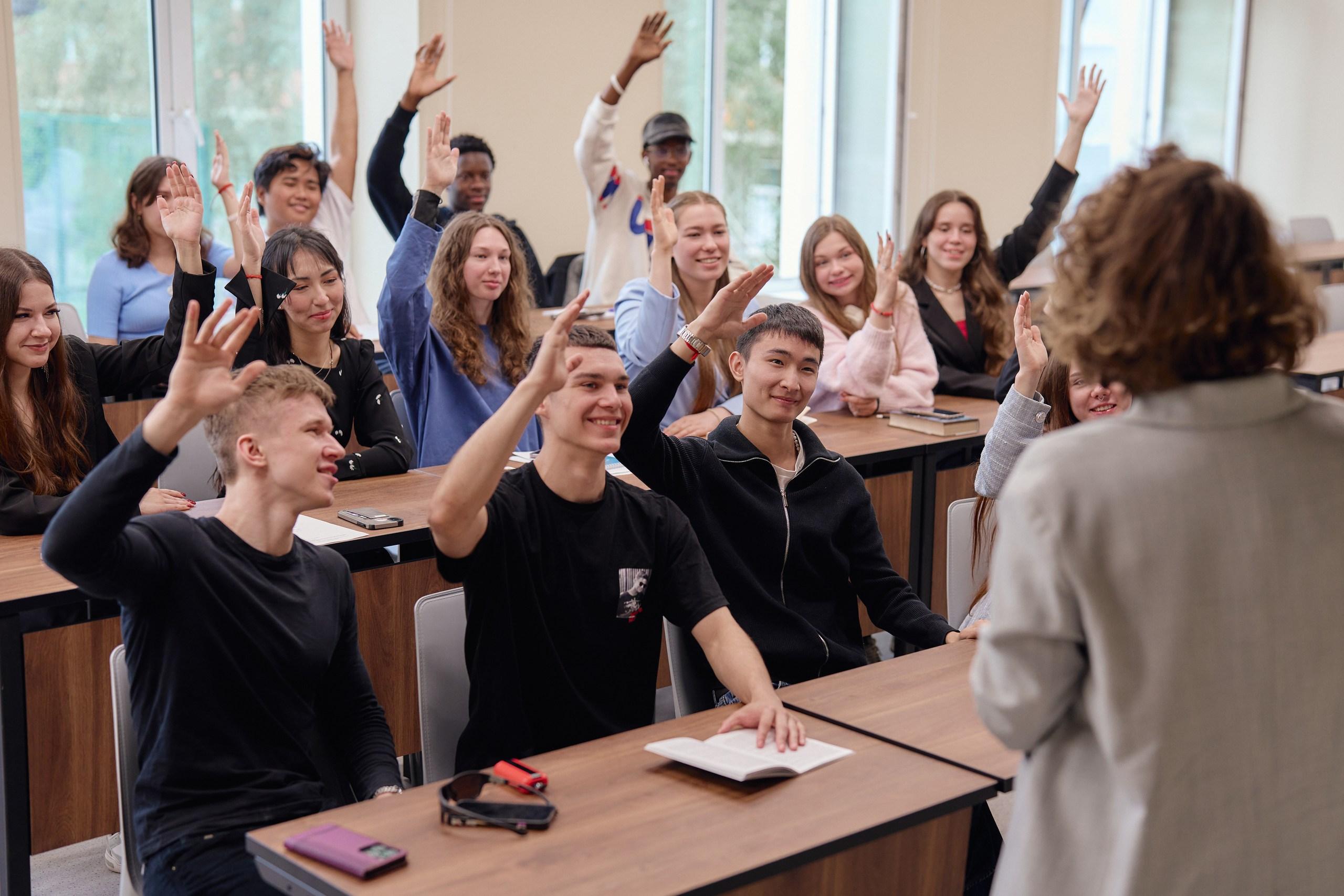 Активные студенты в аудитории поднимают руки, отвечая на вопрос преподавателя.